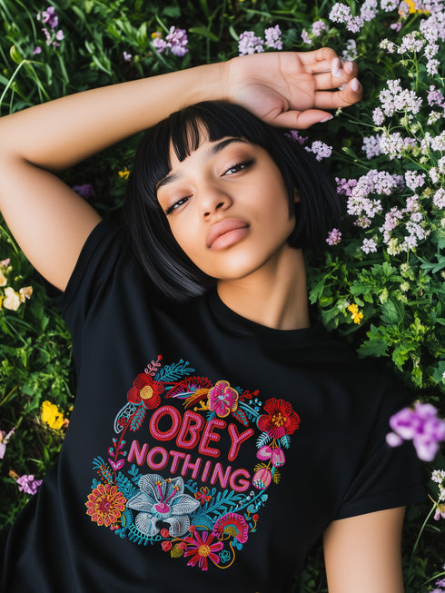 Black activist T-shirt with a floral embroidered-style design and the words “Obey Nothing” in bold, bright lettering.